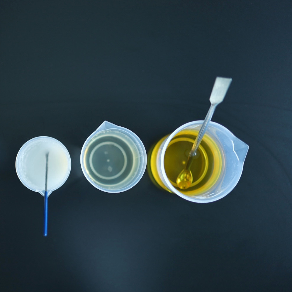 Overhead view of three beakers containing a milky mixture, clear liquid and golden liquid with stirring tools.