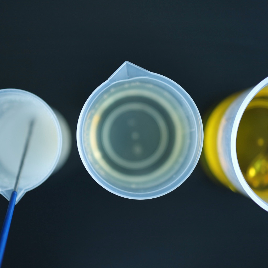 Close-up of beakers containing a milky mixture, clear liquid and golden liquid on a dark surface.