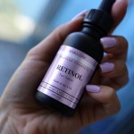 A hand holding a dropper bottle of Elora Clinic Retinol Serum.
